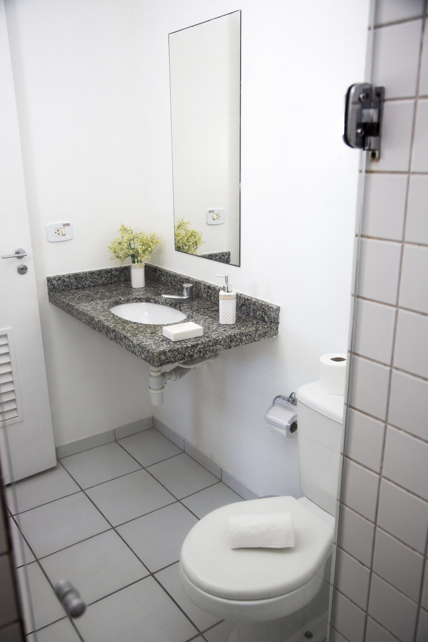 Een kleine badkamer met een wit toilet, een granieten wastafel en een spiegel erboven.