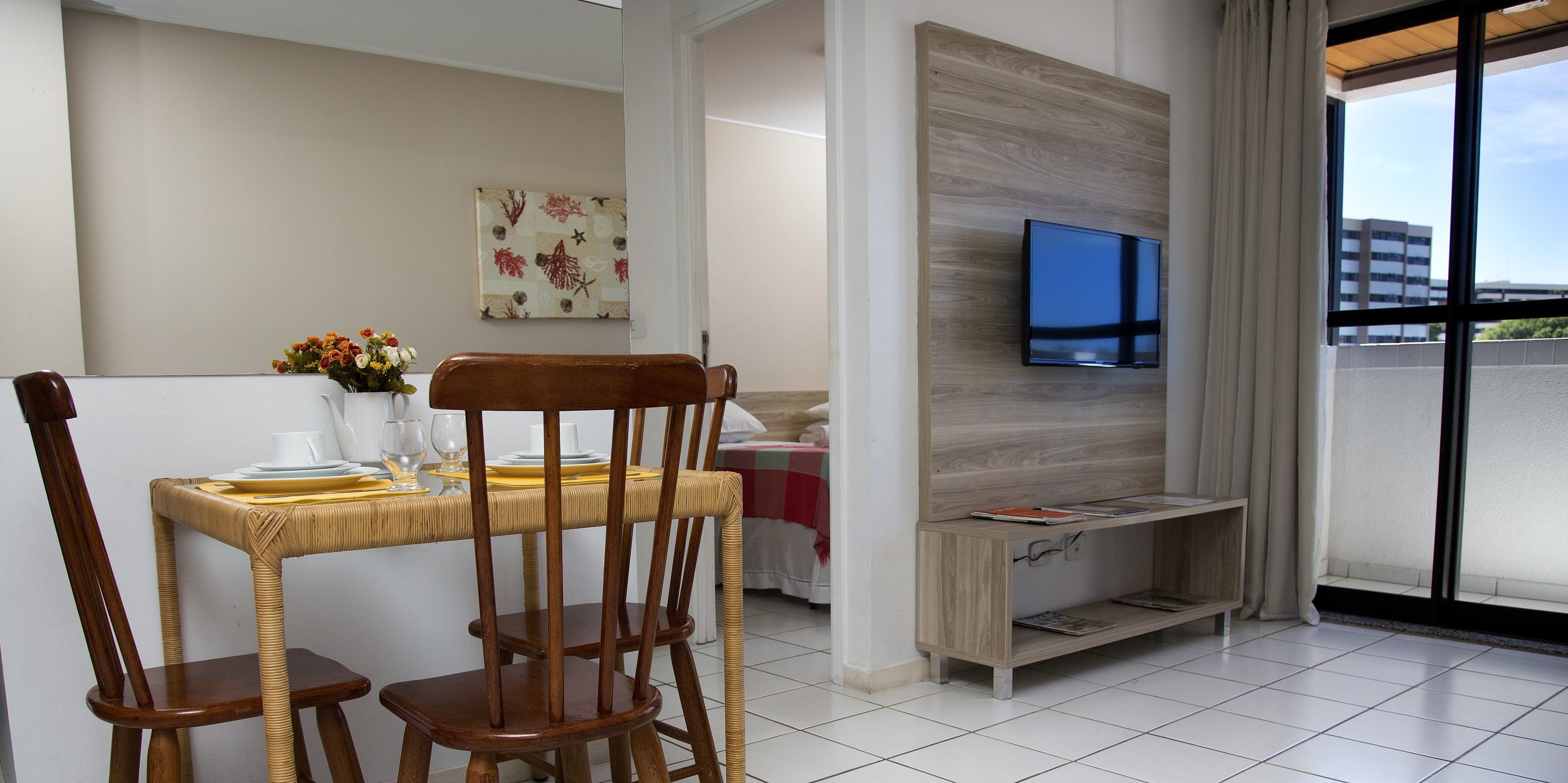 Ein modernes Hotelzimmer mit Essbereich, einem flachbildfernseher an einer Holzvertäfelung und einem großen Fenster mit Blick auf die Stadt.
