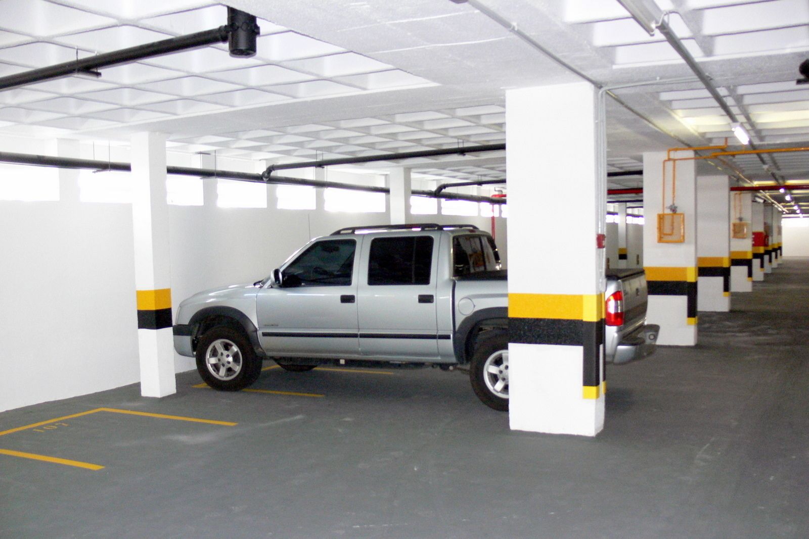 Eine Parkgarage mit weißen Säulen und gelb-schwarzen Markierungen, ein silberner SUV steht in einem Stellplatz.
