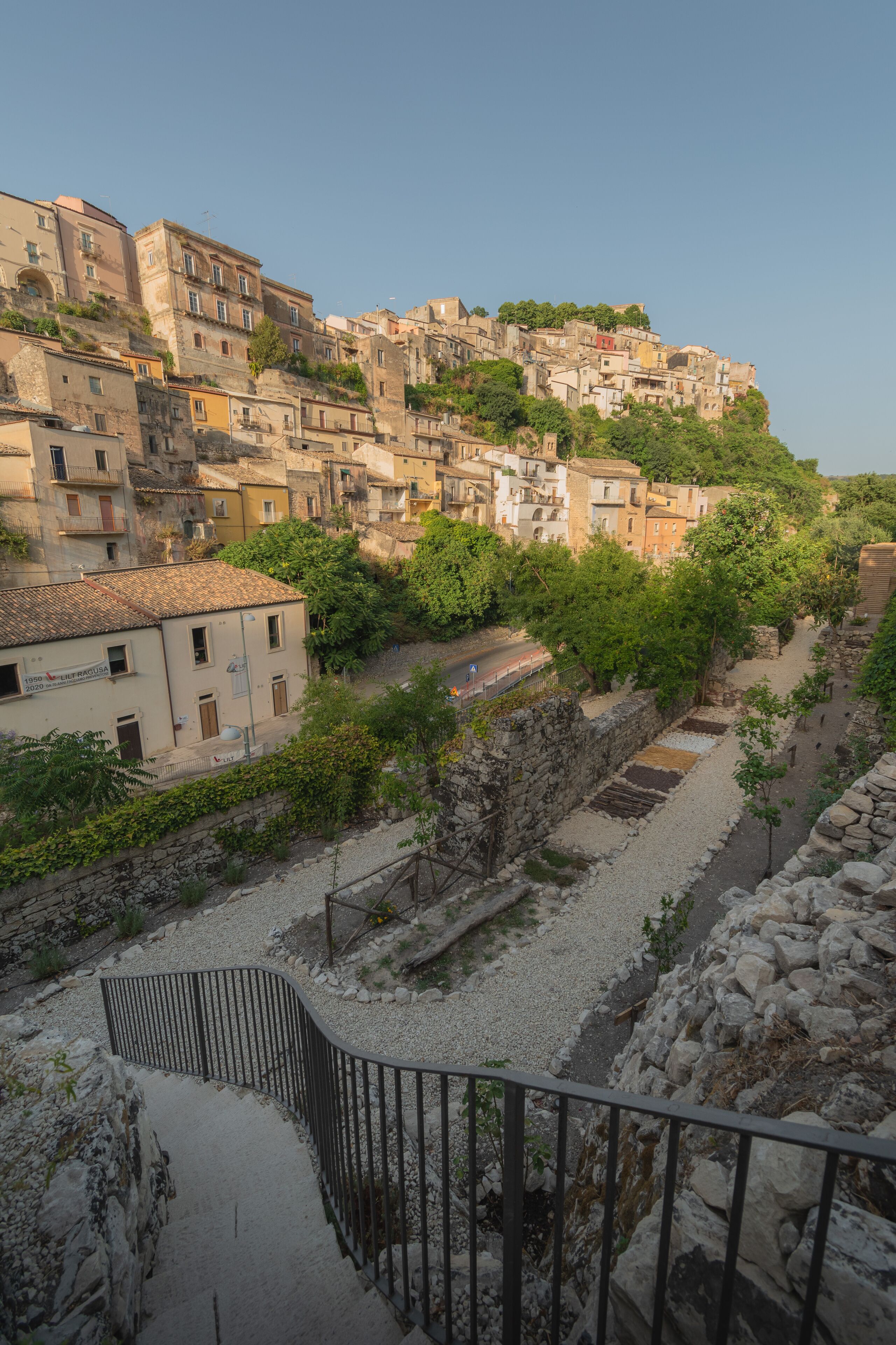 Un poble situat en un turó amb edificis històrics, un camí pavimentat i una paret de pedra.