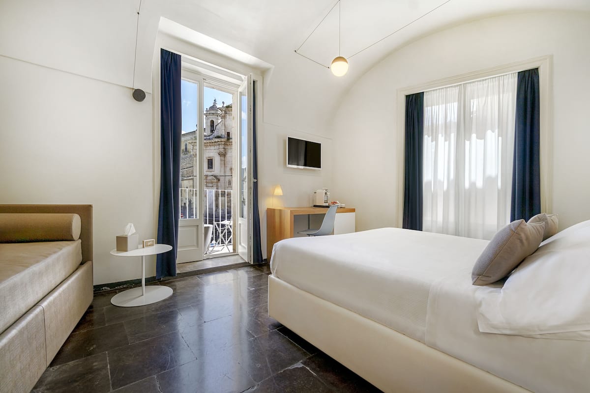 A modern hotel room with a large bed, a desk, a chair, and a small table.