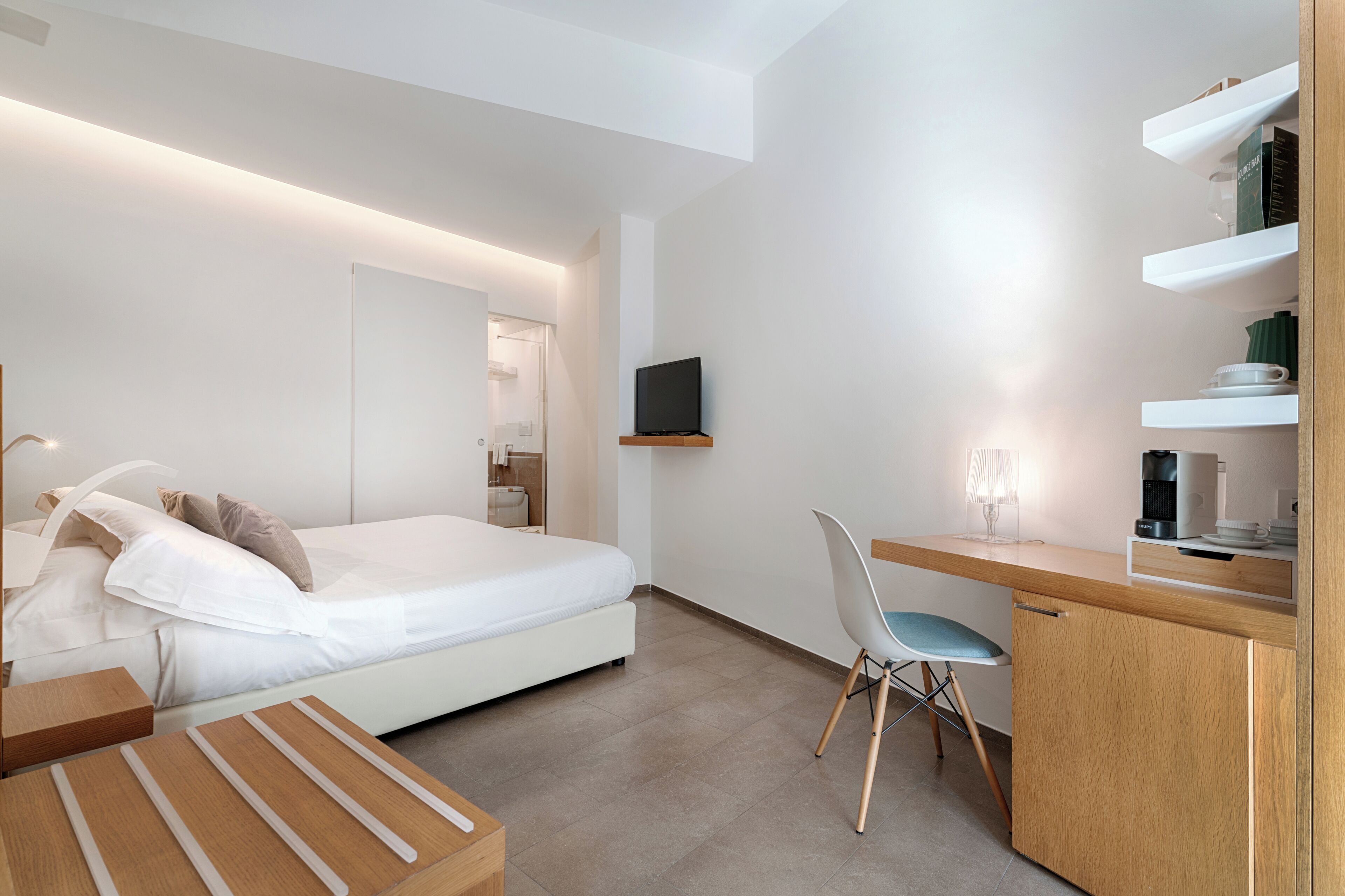 A modern hotel room with a bed, desk, chair, and a TV mounted on the wall.