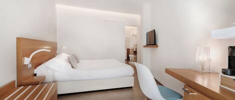 A modern hotel room with a bed, a desk, a chair, and a TV.