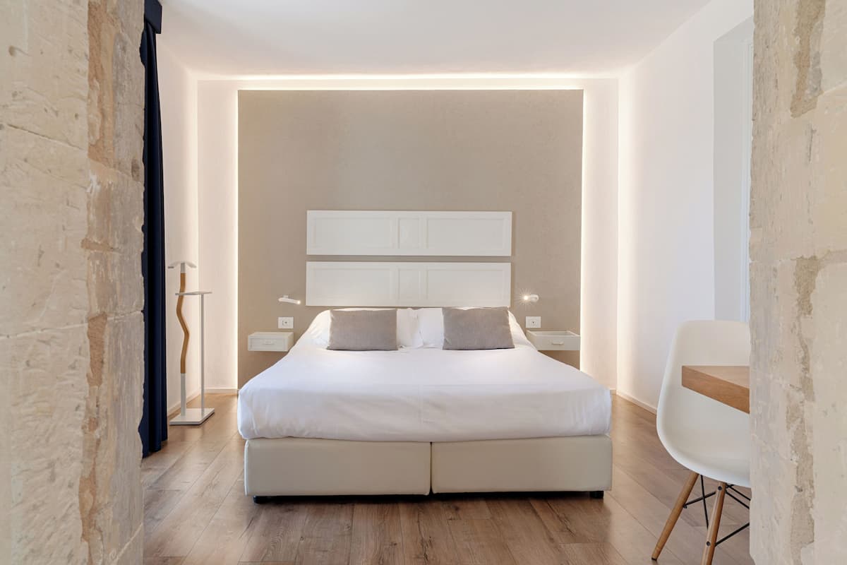 A modern bedroom with a large bed, bedside tables, a chair, and a wooden floor.