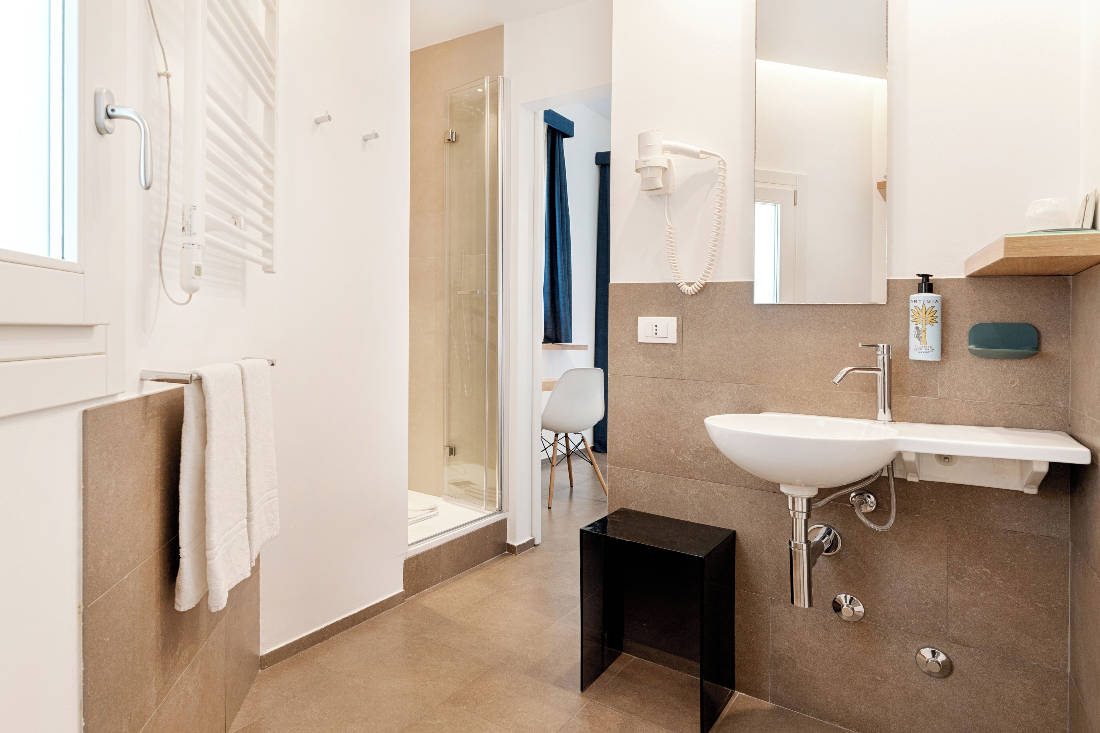 A modern bathroom with a glass shower enclosure, a white sink, and a towel rack.