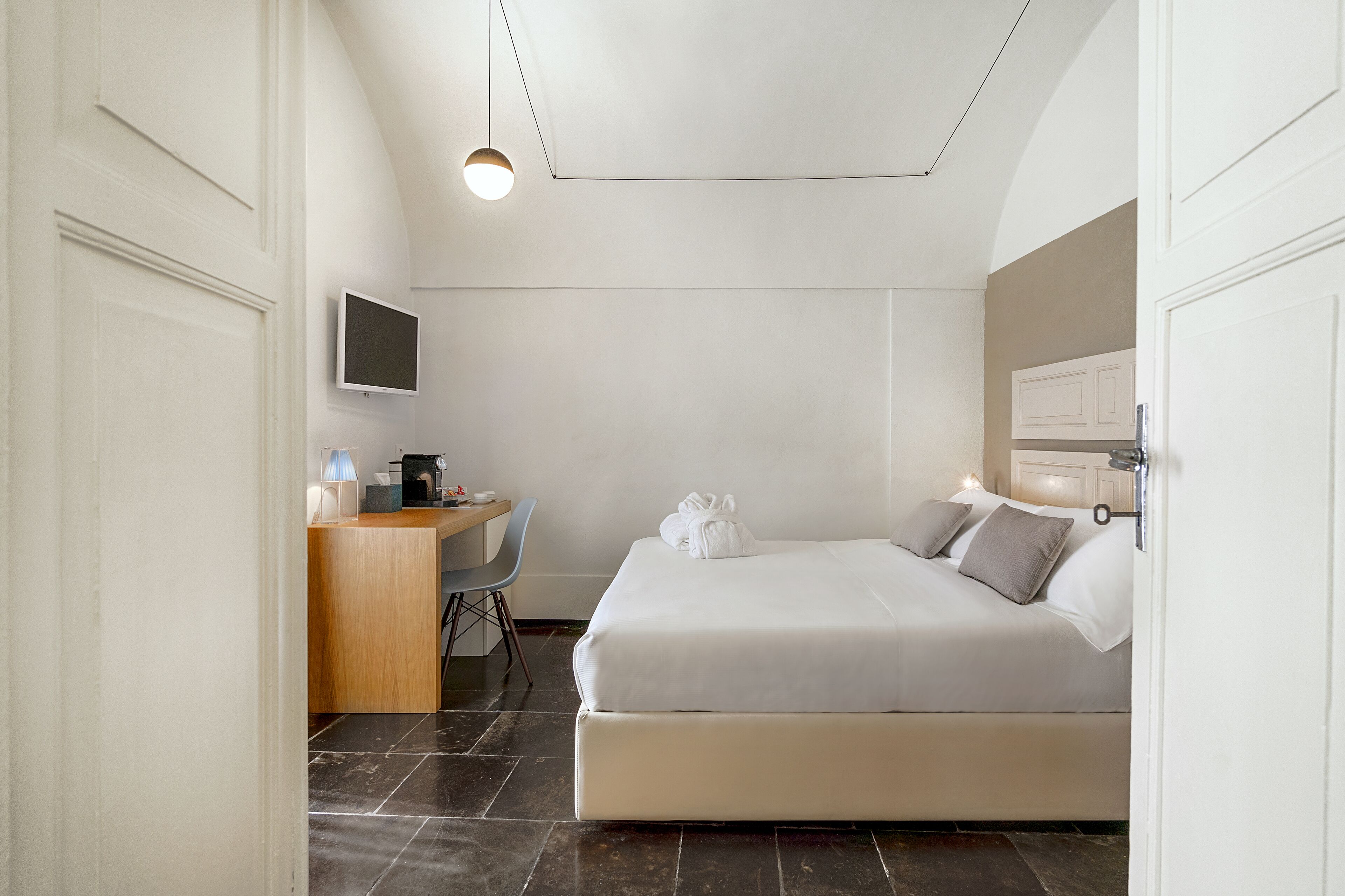 A modern hotel room with a bed, desk, chair, and a flat-screen TV.