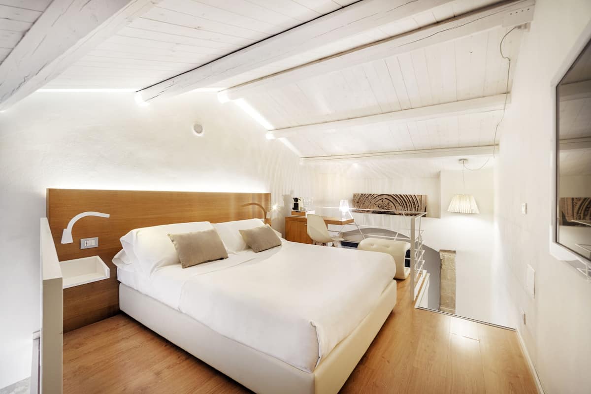 A modern hotel room with a large bed, bedside tables, a desk, and a chair.