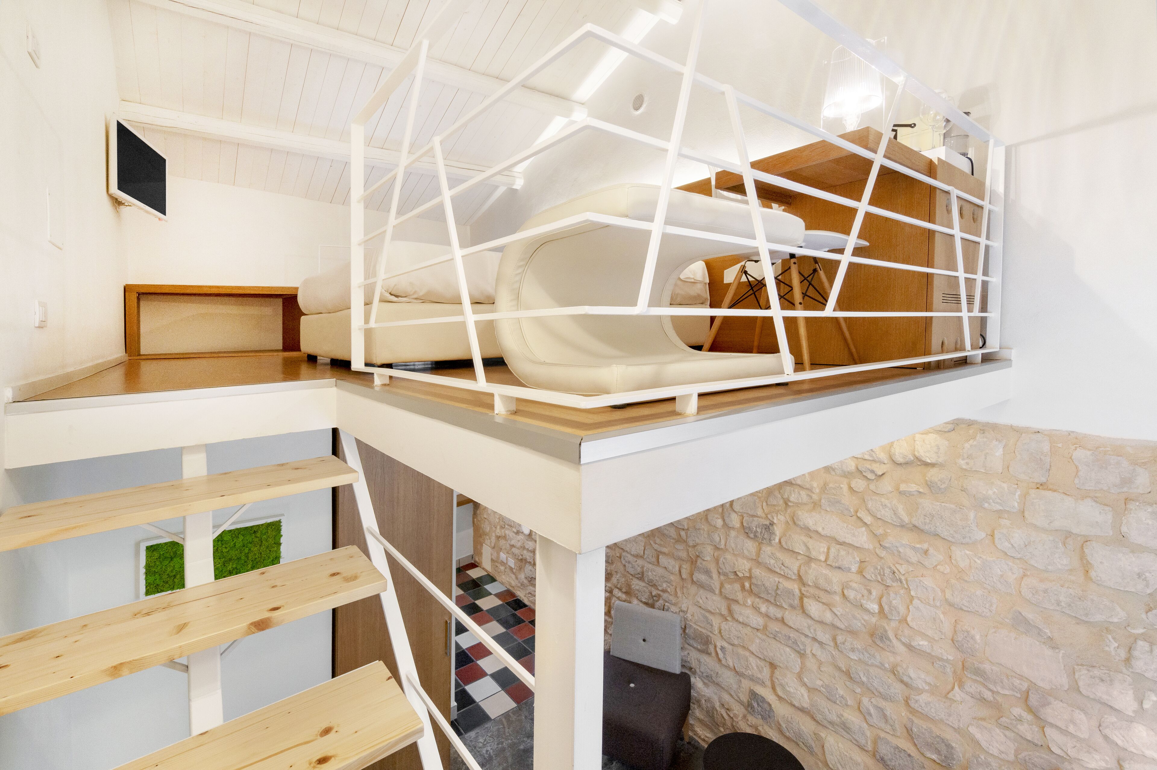 A loft-style bedroom with a bunk bed, a wooden desk, and a stone wall.