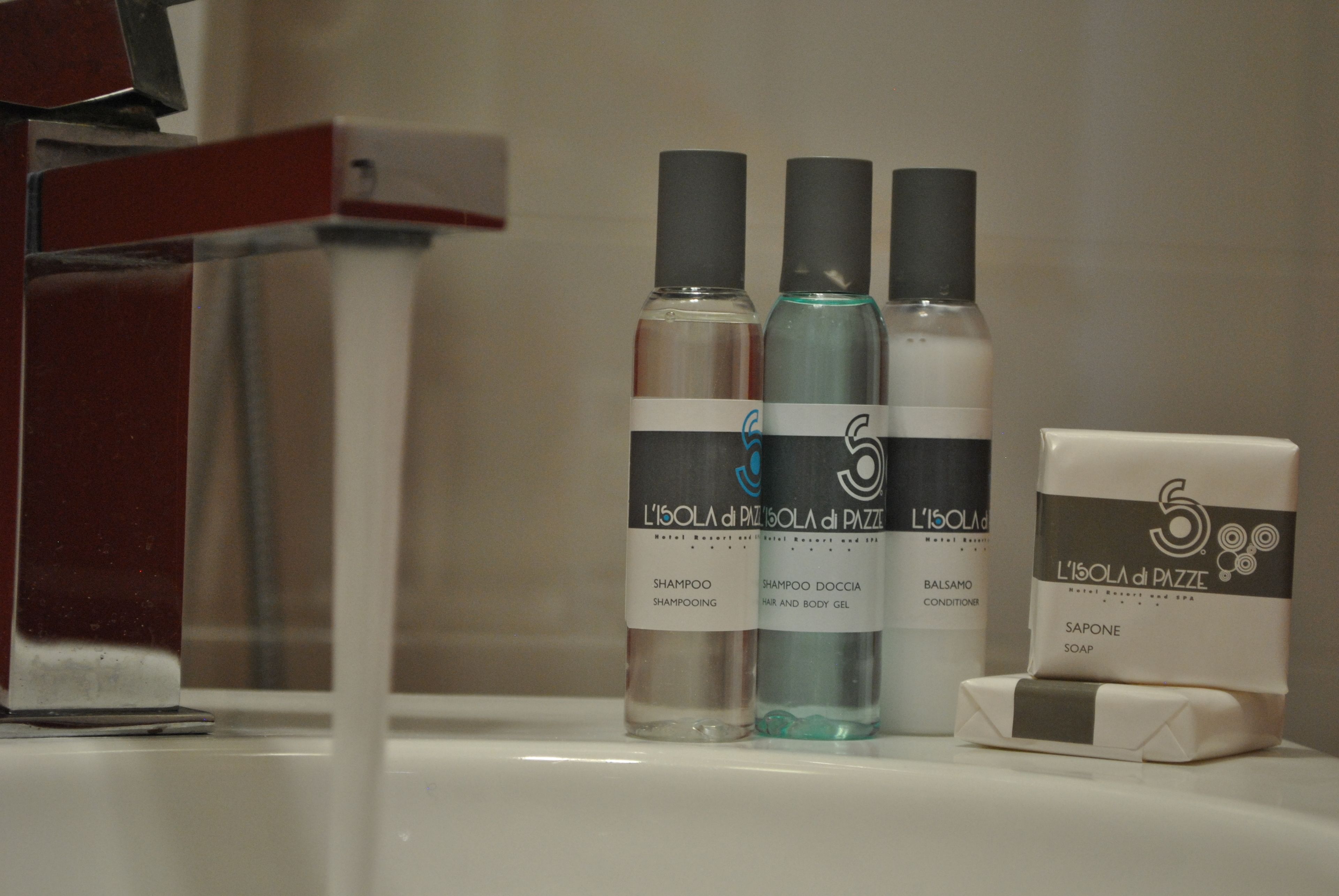 Trois flacons de produits de toilette de l’hôtel L’Isola di Pazzè sont posés sur le comptoir d’une salle de bain.