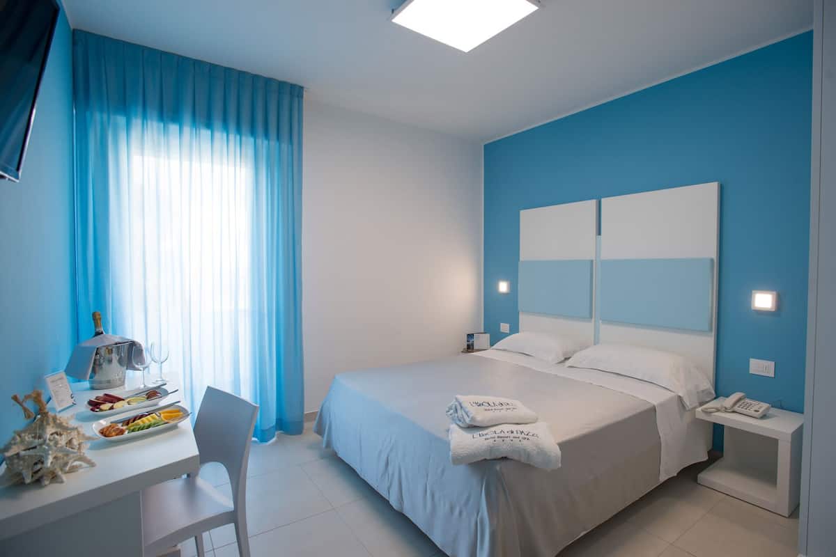 A hotel room with a bed, a desk with a chair, a phone, and a small table with a bottle and glasses.