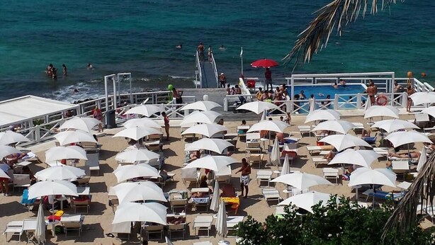 A beachside resort with multiple sun umbrellas and lounge chairs, a pool area, and a view of the ocean. - AH Premium Isola di Pazze (Ugento)