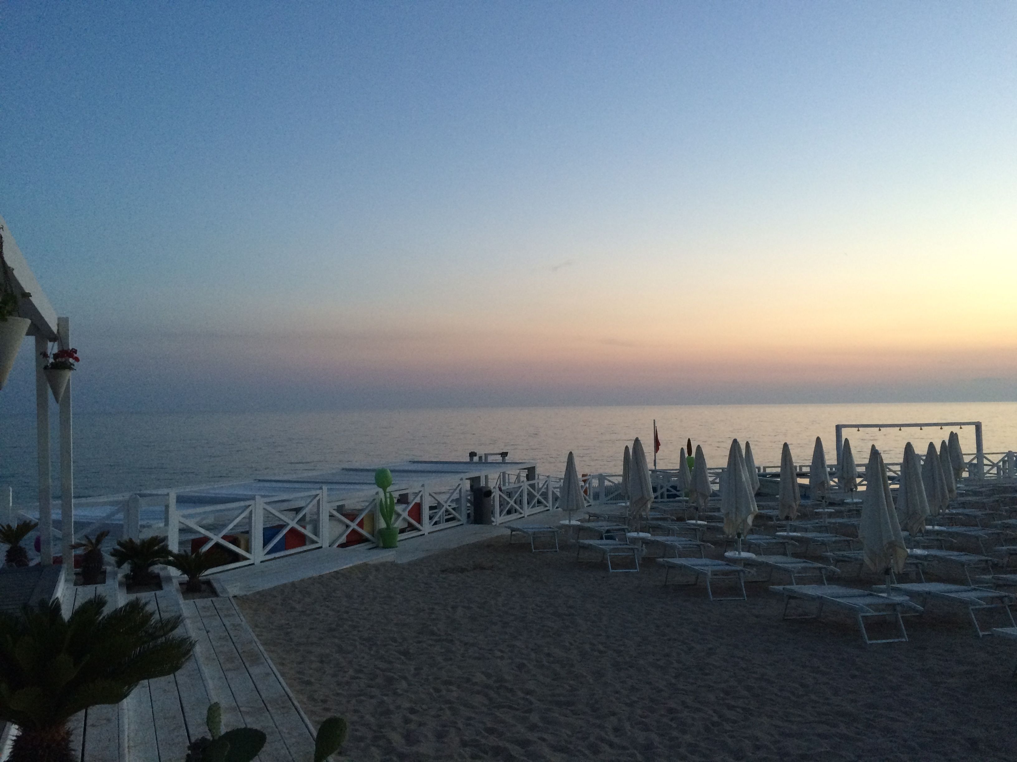 Una spiaggia con una passerella in legno che conduce a una fila di sedie a sdraio e ombrelloni.