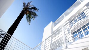 A modern building with white exterior and balconies, palm trees, and a clear blue sky. - AH Premium Isola di Pazze (Ugento)
