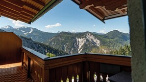 A wooden balcony with a view of snow-capped mountains and forested valleys.