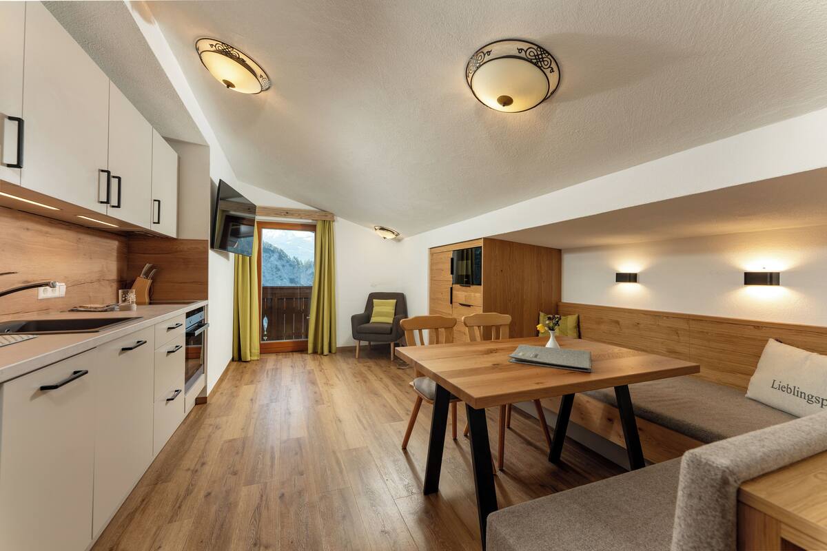 Une cuisine moderne avec des meubles en bois, un four encastré et un évier. On y trouve également un coin repas avec une table et des bancs en bois.