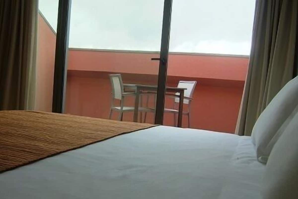 Ein Hotelzimmer mit einem Bett, Blick auf den Himmel und einem Stuhl vor dem Fenster.