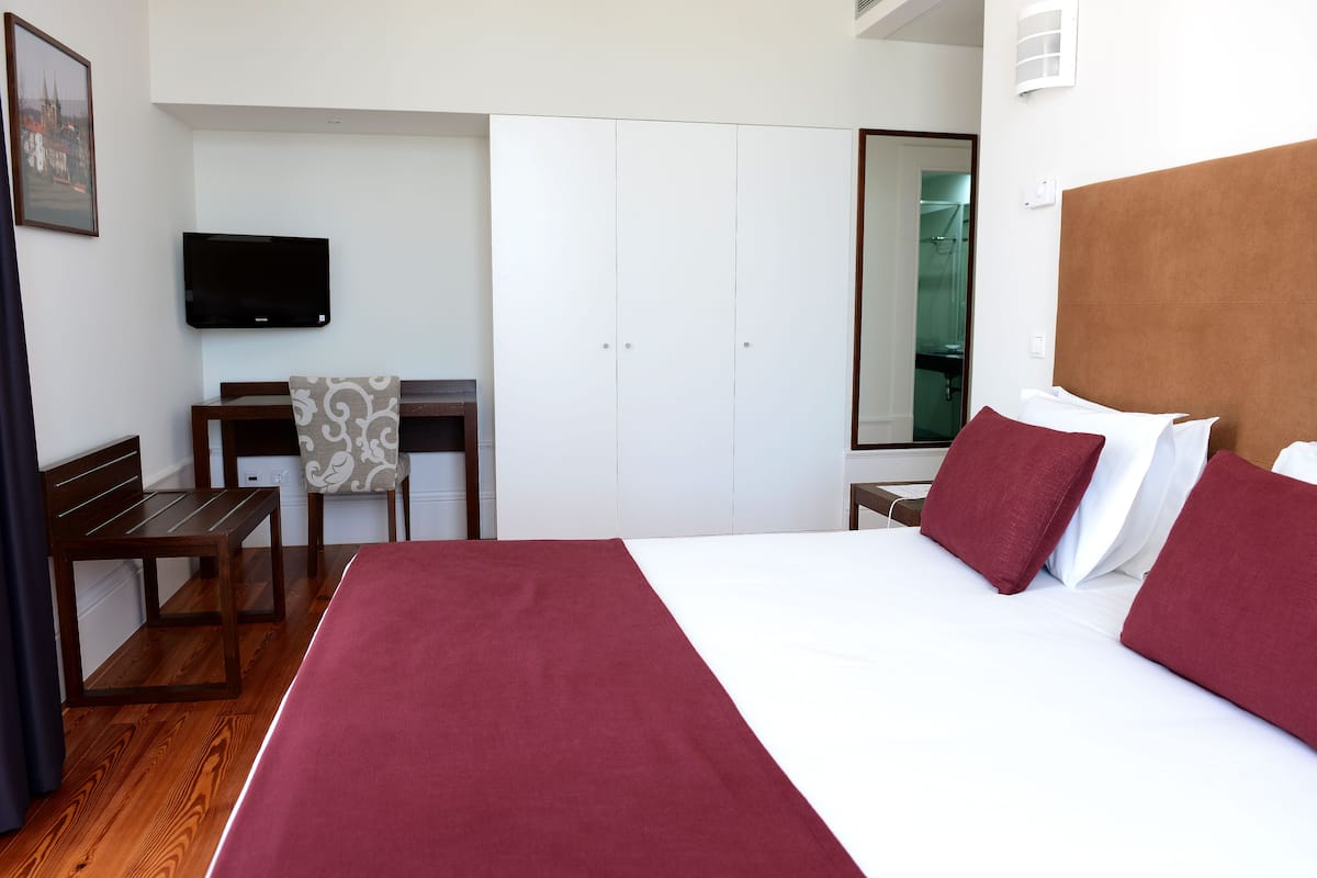 Ein Hotelzimmer mit Bett, Schreibtisch, Sessel, Fernseher und Kleiderschrank.