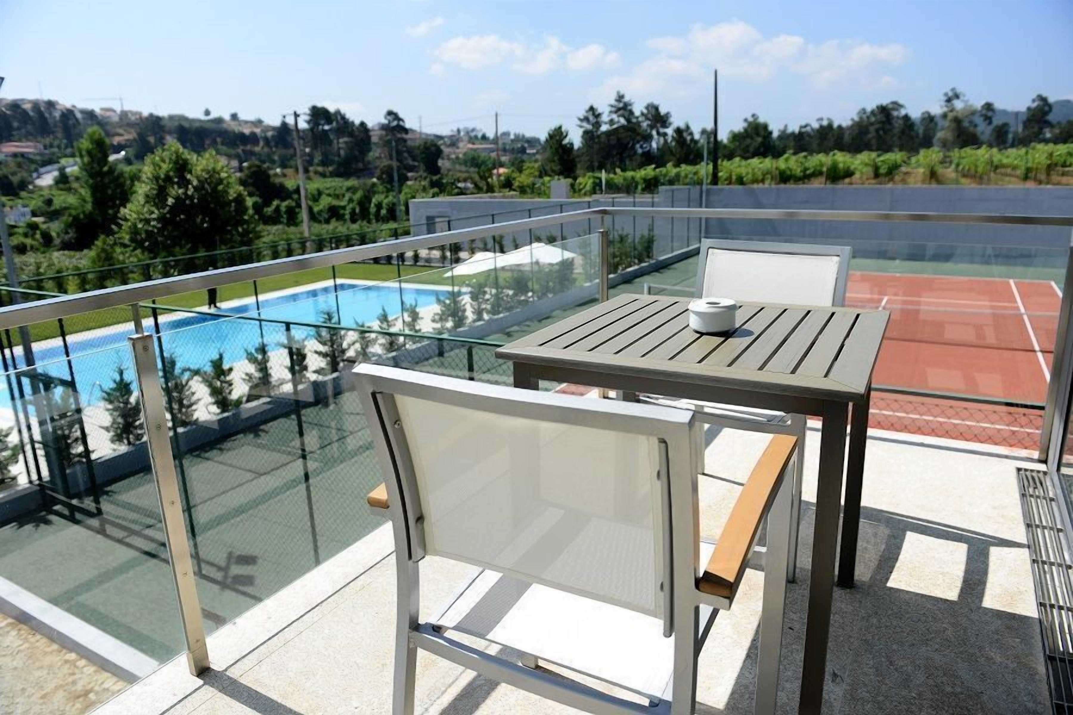 A balcony with a glass railing, a pool, and a tennis court.