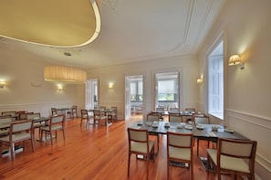 A spacious conference room with wooden tables and chairs, large windows, and wall-mounted lamps. - Hotel Rural Quinta Da Cruz (Amarante)