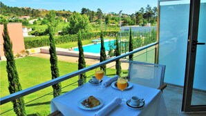 A balcony with a table set for breakfast, overlooking a swimming pool and lush greenery. - Hotel Rural Quinta Da Cruz (Amarante)
