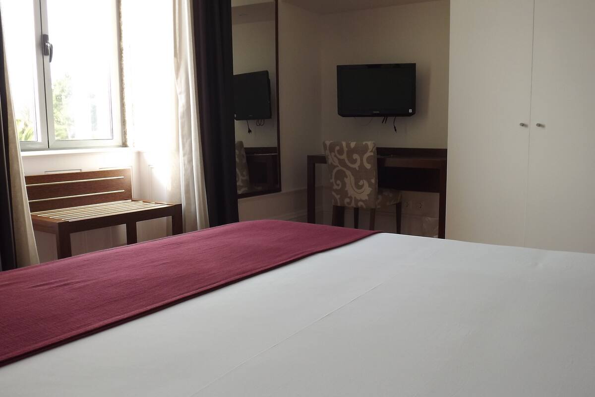 Ein Hotelzimmer mit Bett, Schreibtisch, Stuhl, Fernseher und Kleiderschrank.