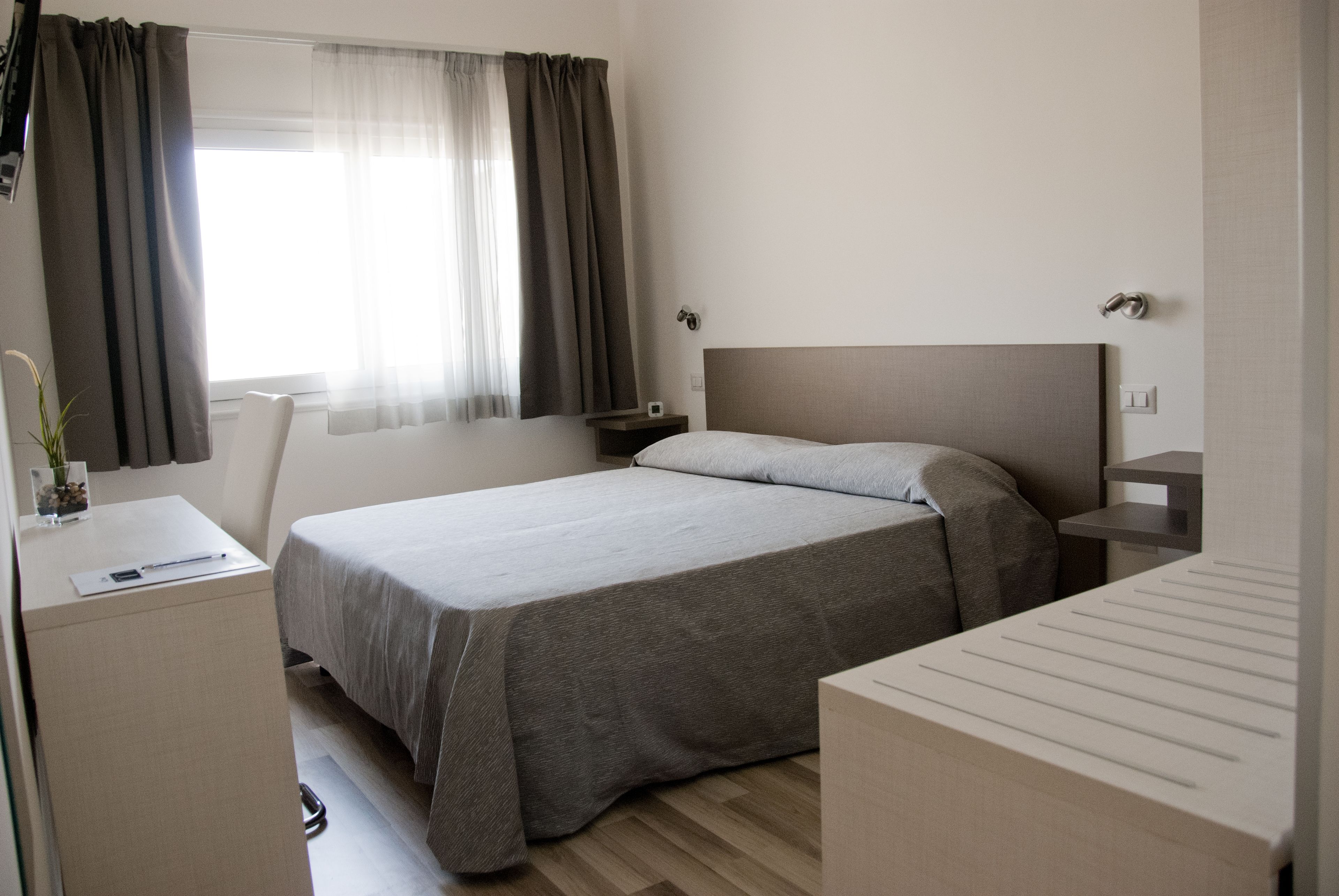 Ein Hotelzimmer mit Bett, Nachttischen, Schreibtisch und einem Vorhangfenster.
