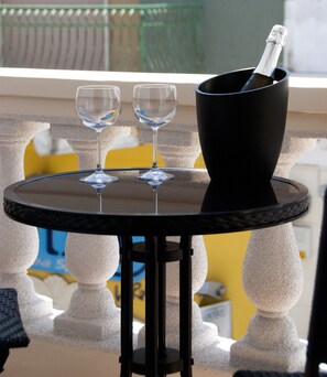 A table with two wine glasses and a champagne bottle in a black holder, set on a balcony with white balustrades and yellow chairs. - Il Corso (Porto Cesareo)