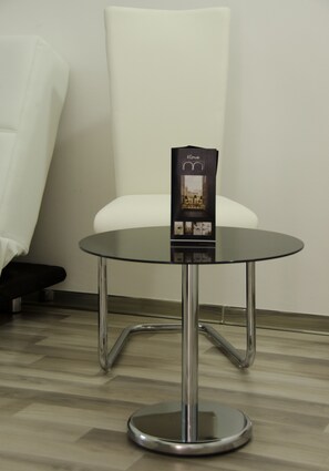 A round glass table with a metallic base, a white chair, and a small black object on the table. - Il Corso (Porto Cesareo)