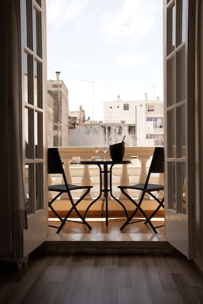 Un balcón abierto con dos sillas y una mesa, con vistas a un paisaje urbano.