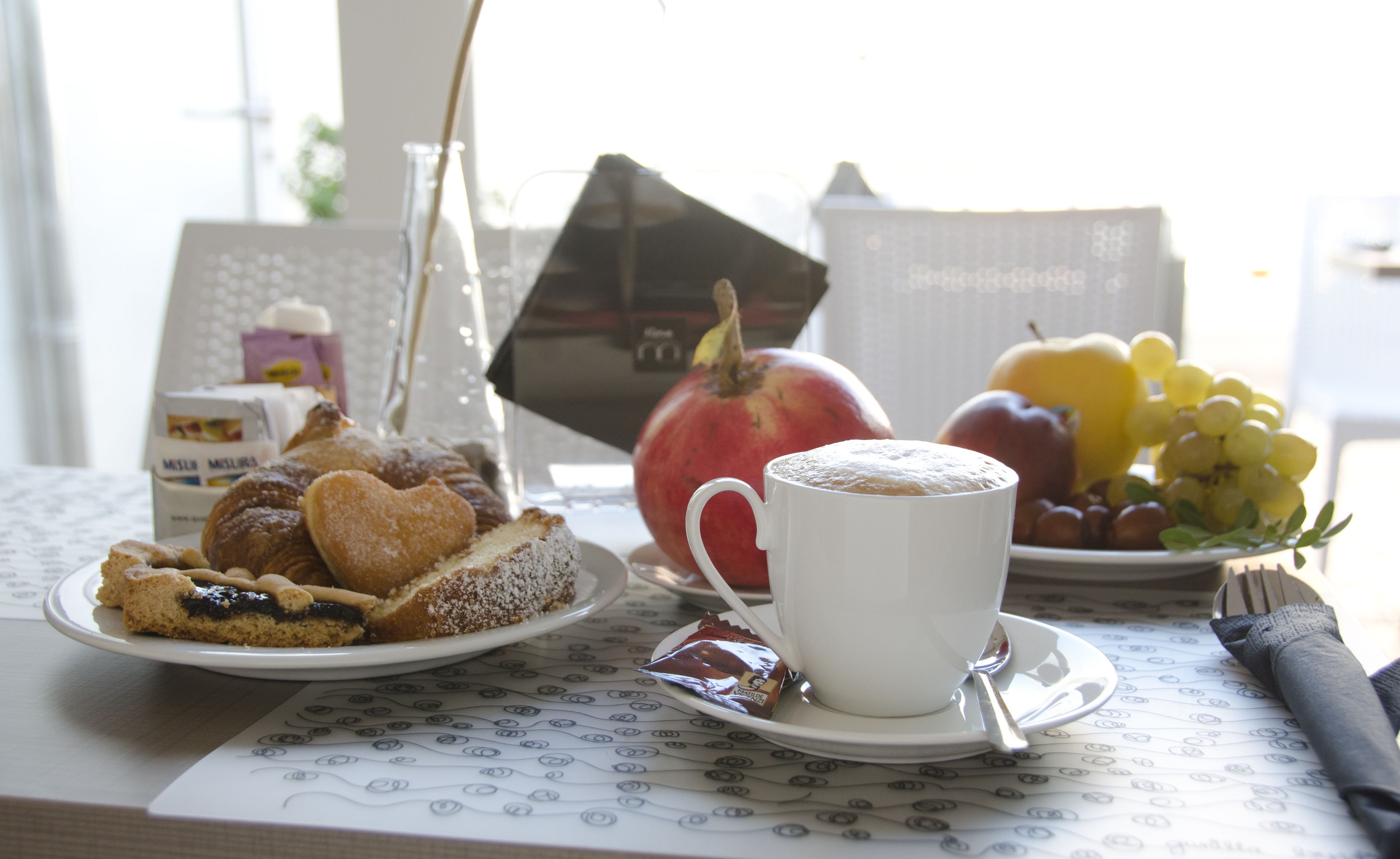 A breakfast table with pastries, a cup of coffee, and a plate of fruit.