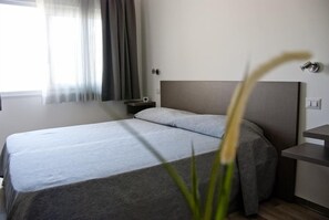 Habitación de hotel con cama, mesita de noche, lámpara y ventana con cortinas.