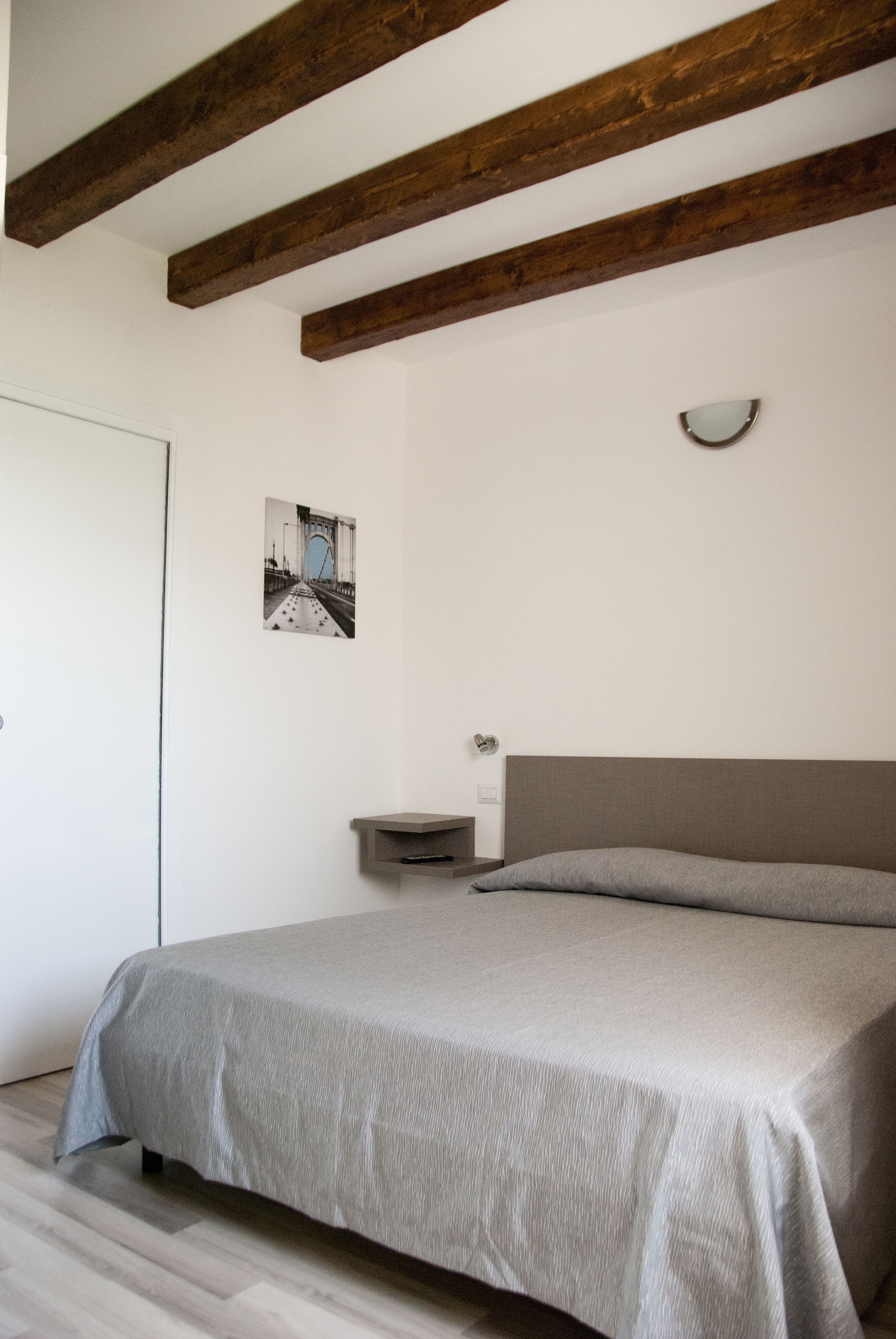Ein Schlafzimmer mit einem Bett, Holzbalken, einem Nachttisch, einer Wandleuchte und einer Tür.
