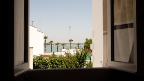 A view through a window of a coastal area with buildings, palm trees, and a clear sky. - Il Corso (Porto Cesareo)