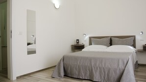 A bedroom with a bed, bedside tables, a mirror, and a wall-mounted light fixture. - Il Corso (Porto Cesareo)