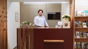 Un comptoir d'accueil avec un panneau décoratif en bois, une orchidée en pot et une étagère contenant des livres et un tableau encadré.