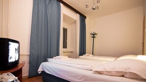 A hotel room with a bed, a television, a coat rack, and a window with curtains. - Pension Nika (Prague)