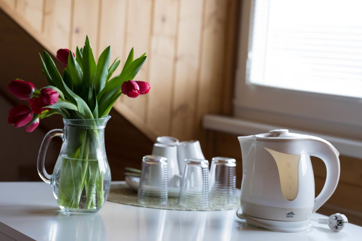 A clear glass pitcher with tulips, a white electric kettle, and stacked glass cups on a table.