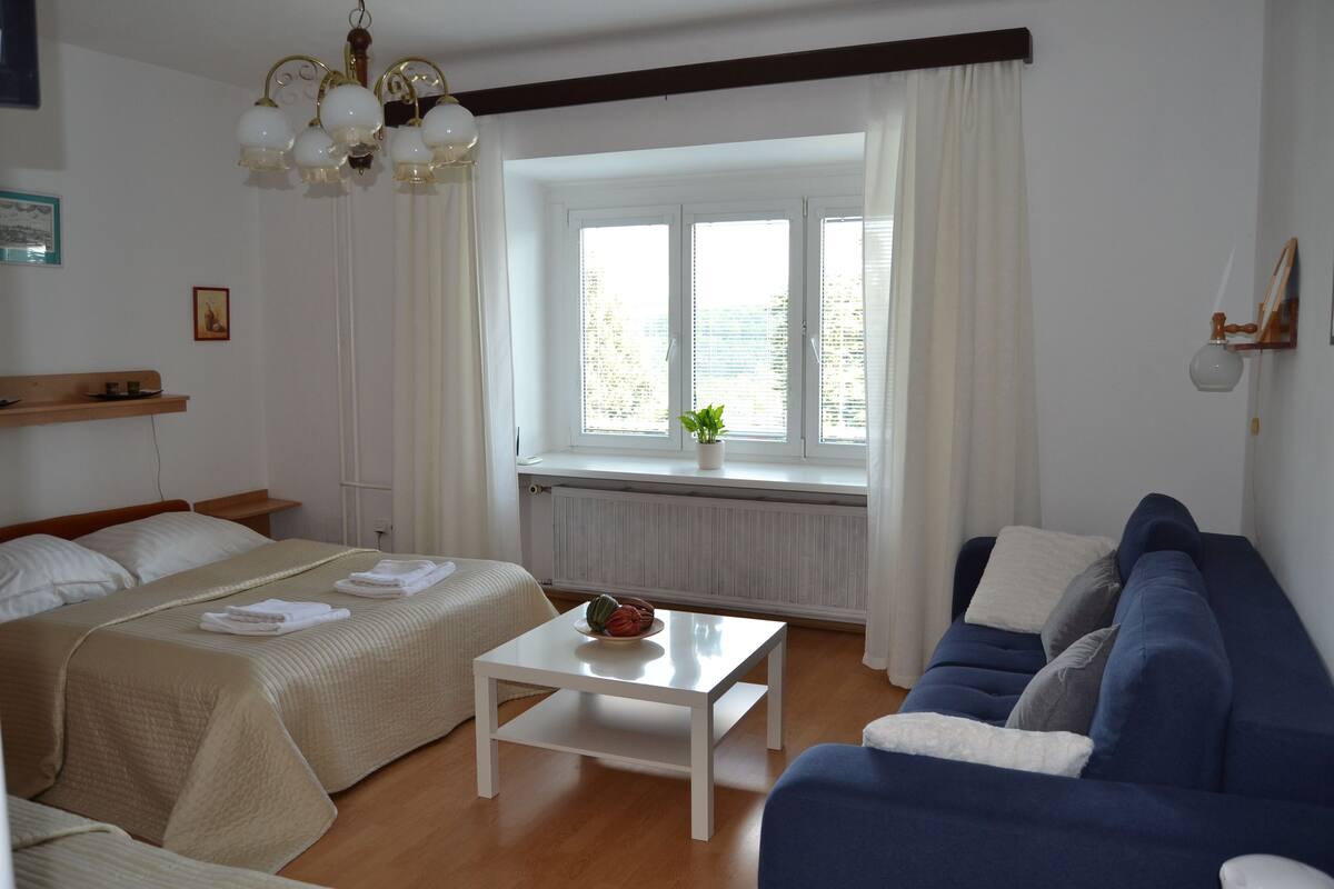 A room with two beds, a blue sofa, a white table, and a window with curtains.