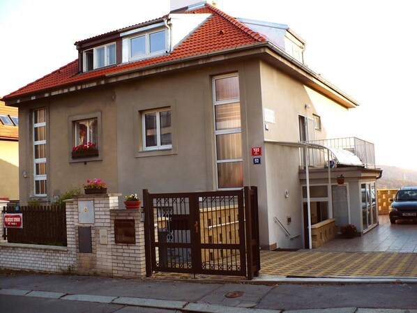 A two-story building with a red-tiled roof, a gated entrance, and a balcony.