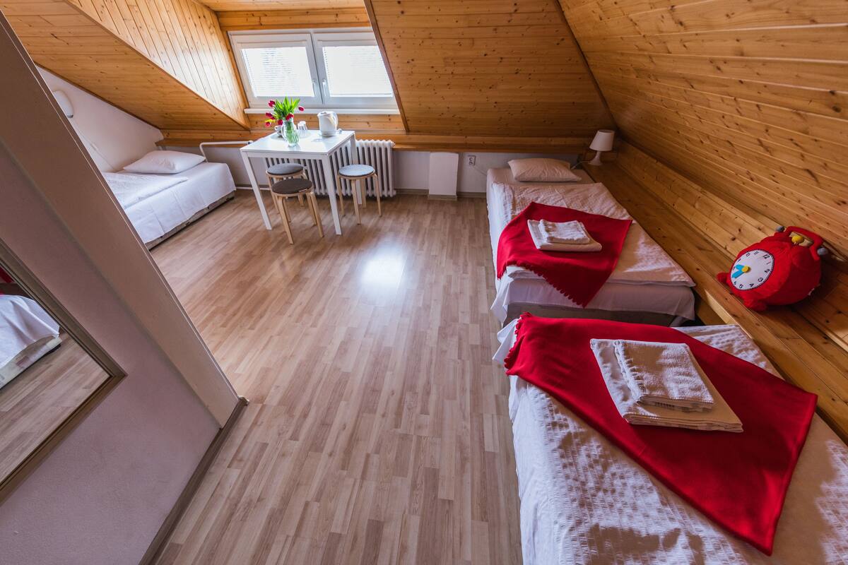A cozy attic room with two beds, a dining table, and a red alarm clock.
