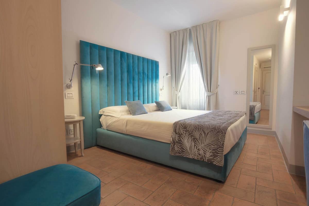 A bedroom with a bed, bedside tables, a mirror, and a window with curtains.