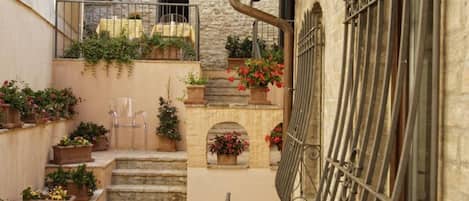Un estrecho patio con escalones de piedra, plantas en macetas y mobiliario de exterior.