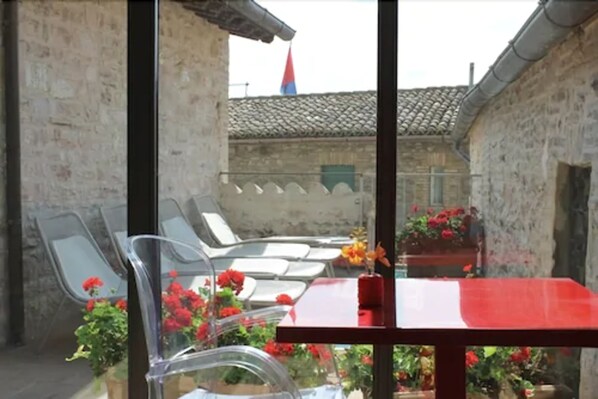 Un patio con una mesa y sillas rojas, rodeado de muros de piedra y plantas en macetas.
