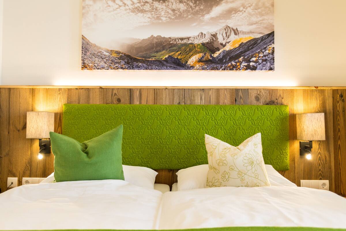 A bed with white linens and green pillows, a green headboard, and a wall-mounted lamp.