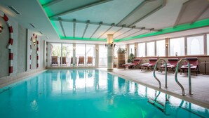 An indoor swimming pool with clear water, a ceiling with green lighting, and sunlit windows. - Hotel Alte Schmiede (Seefeld in Tirol)