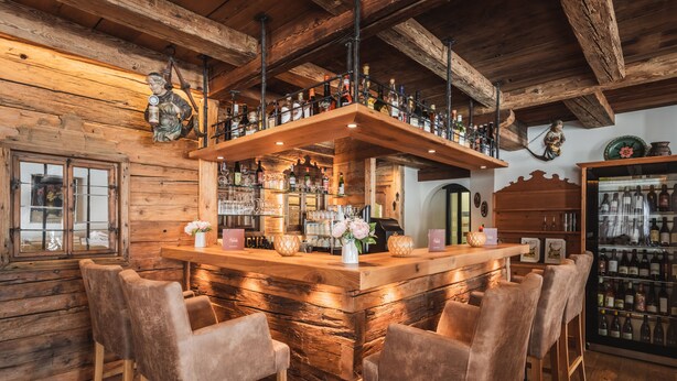 A rustic bar area with wooden walls, a wooden bar counter, and bar stools. - Hotel Alte Schmiede (Seefeld in Tirol)