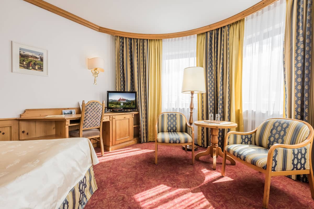 A hotel room with a bed, a desk, a television, a chair, a sofa, and a lamp.