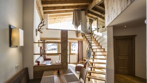 A spacious room with a wooden staircase, a dining area with a table and chairs, and a large window providing a view of the outside. - Hotel Alte Schmiede (Seefeld in Tirol)
