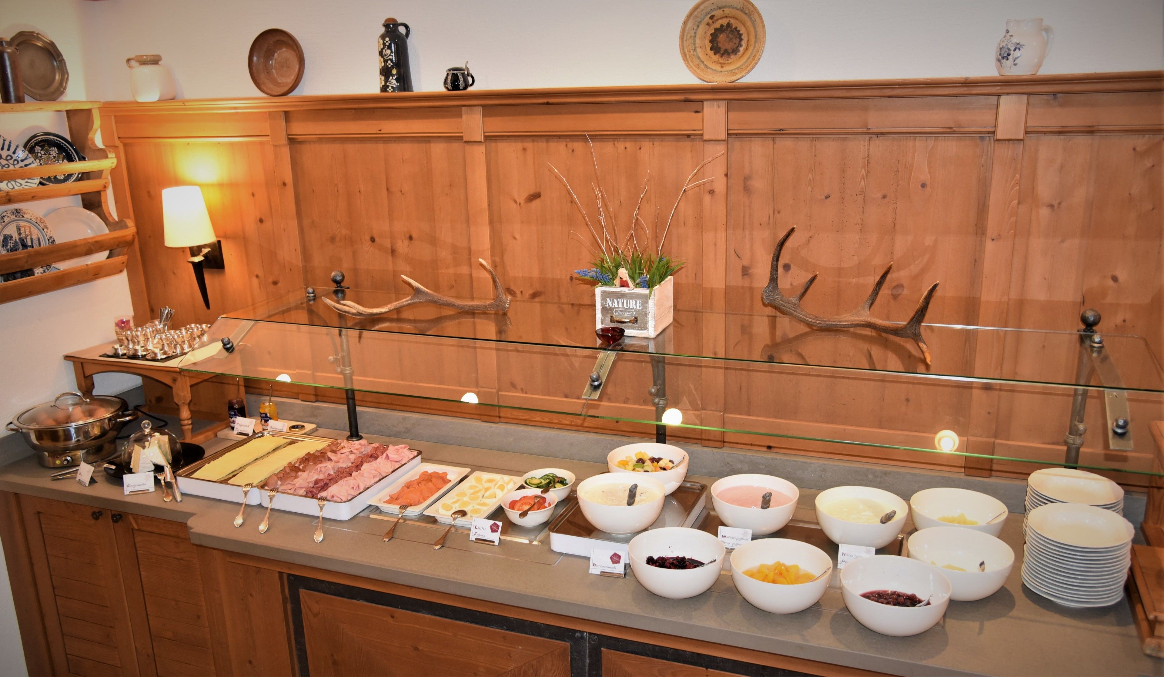 A buffet with various food items and a wooden wall with decorative antlers.