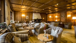 A cozy, wood-paneled room with multiple seating areas, including sofas and armchairs, arranged around a central fireplace. - Hotel Alte Schmiede (Seefeld in Tirol)